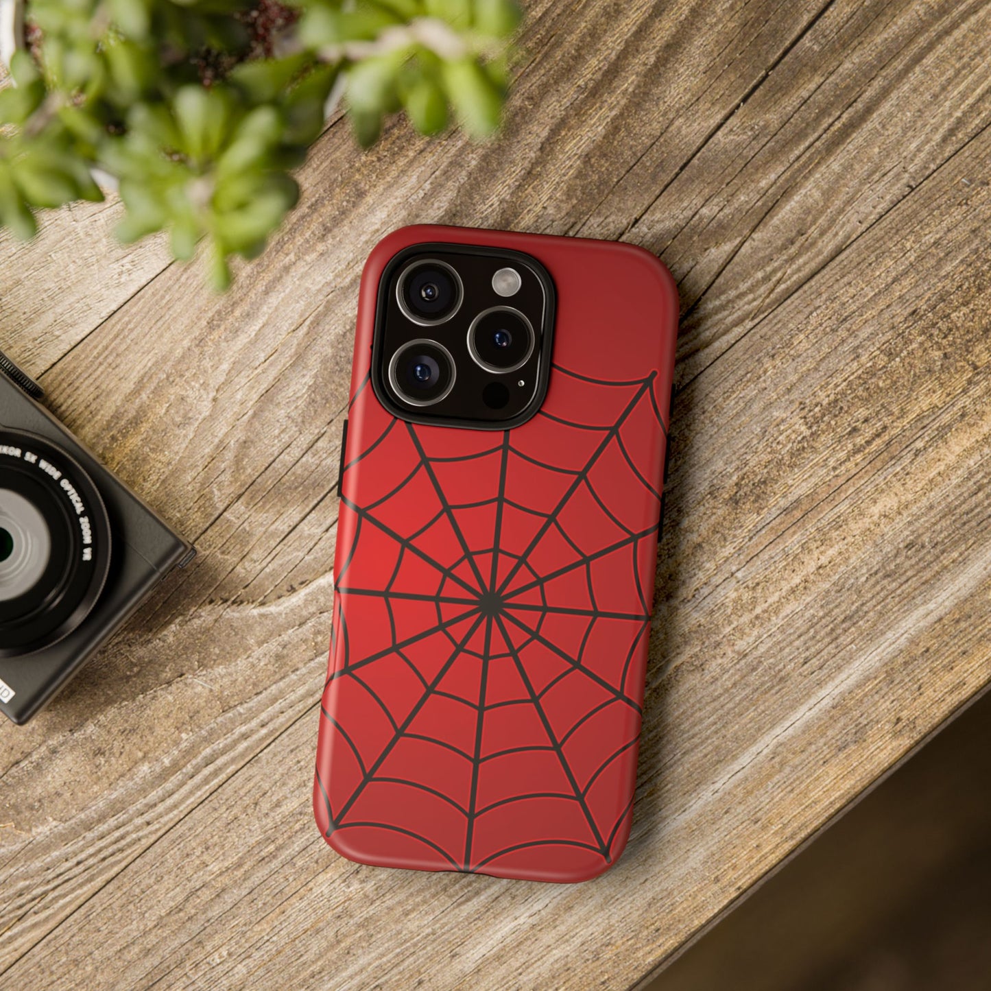 Lifestyle flatlay of red spiderweb iPhone case on wooden surface – bold superhero-inspired phone cover for comic lovers and stylish everyday use